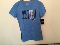 Front view of light blue Nike T-shirt with "JUST DO IT" graphic and hang tag