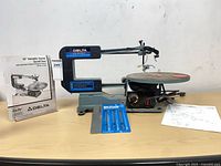 Full view of Delta 40-540 scroll saw with manual, blades pack and schematic on table