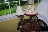 Two lamps on a wooden side table by a window. Each lamp has a separate fabric shade and clear glass globes in front of them.