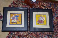 Two framed Art Deco folk art paintings depicting Russian costumes, each 12x12 with cream matting and black frame.