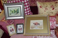 Four framed fruit prints displayed on a sofa with patterned pillows, each depicting different fruit including apples, oranges and plums
