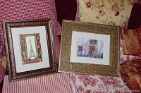 Two framed prints displayed on a floral patterned fabric surface: one with the Eiffel Tower illustration and the other a courtyard scene.