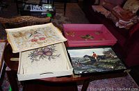 Four painted serving trays shown on a table, various designs in pink, white with fruit, cream crackled with flower, and black with hunting scene