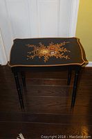 Full view of black wooden side table with floral painted design on top.