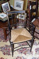 Antique wooden armchair with rush seat showing overall wear and siting among other framed artworks and furniture.
