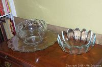 Photo of clear crystal punch bowl on glass plate with scalloped edges and teardrop glass embellishments on the bowl rim, placed on wooden chest.