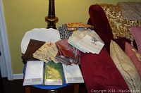 Collection of assorted dinner napkins and hand towels stacked on a table and sofa arm.