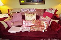 Photo of red sofa with assorted pillows, folded fabrics, tablecloth and textile pieces