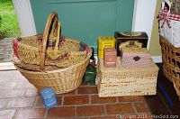 Stacked three nested wicker baskets on floor beside various decorative tins and a rectangular woven box with lid.