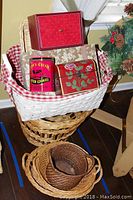 Photo of assorted baskets stacked and arranged, showing the wicker laundry basket, white basket with tins, and smaller baskets on a wooden floor.