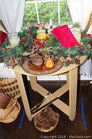 Overall view of Christmas pine wreath on wooden tray and foldable table with candles, napkin, and basket with pinecones below.