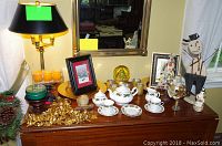 Full view of Christmas decor arrangement including holly tea set, snow globe, snowman figurine, framed pictures, and lamp on wooden surface.