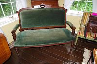 Front view of Victorian loveseat showing green velvet seat and backrest with carved wooden frame and legs.