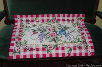 Full view of the hooked rug showing floral design and checkered border on a dark green sofa.