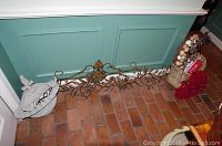 Decorative metal wall piece lying on a brick floor against a teal wall, featuring scrollwork and leaf designs