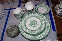 Green patterned Nikki plateware set with plates, cups, saucers and coasters arranged on a table.