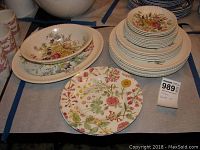 Overview of dinnerware including stacked plates, platters, bowl, and mugs featuring floral Garden Bouquet pattern