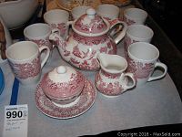 Full set of red transferware items including teapot, mugs, creamer, sugar bowl with lid and plate arranged on table.