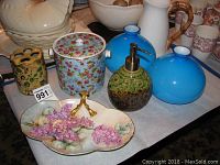 Photo showing multiple items including a ceramic pitcher with bamboo-look handle, large floral covered jar, two blue glass vases, green soap dispenser, yellow floral holder, and the Limoges candy dish with floral painting and gold handles