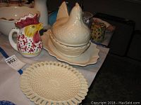 Rooster-shaped pitcher, chicken serving dish with lid, ceramic bowl, and faux brown eggs displayed.