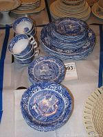 Overview of stacked plates, cups, and saucers showing traditional blue and white Spode Italian design pattern with scenic imagery and floral borders.