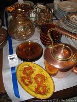 Marigold carnival glass pitcher with grape and floral design, amber glass bowls and plates, copper kettle, and French redware platter on table.