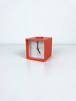 Front view of red cube alarm clock showing dial and hands