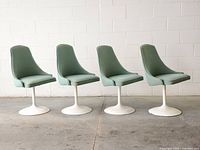 Four teal upholstered swivel tulip chairs with white bases, side view