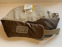 Full view of massager cushion with straps, cord and tag