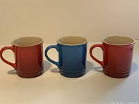 Three Le Creuset mugs upright, exterior colors visible