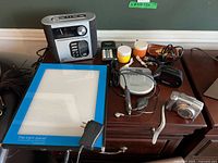 Overview showing Timex clock radio, batteries, film canisters, cables, Sony Discman, Panasonic charger, speakers, light panel and Canon camera