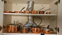 Cabinet view showing entire lot of copper pots and pans on two shelves