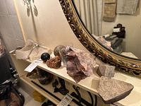 Shelf showing multiple rock specimens, glass tumbler with crystals, marble sphere, fossil fragment, large mineral chunk