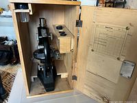 Microscope inside wooden case, shelf with two eyepieces and vial visible