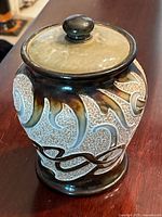 Front view of lidded stoneware tobacco jar showing raised slip decoration and glaze