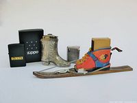 Group shot of all four items: boxed DeWalt Zippo lighter, Concorde lighter, Occupied Japan boot figurine, Austrian ski match holder
