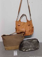 Front view of three handbags: tan Fossil, brown Coach, gray Coach