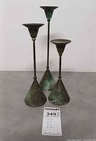 Frontal view of three patinated candle holders with measurement card