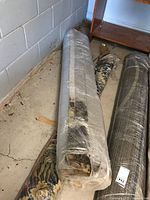 Rolled rug wrapped in plastic mesh next to other rugs