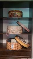 Three decorative hat boxes on shelving, one open showing hats inside