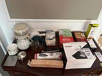 All items arranged on dresser: boxed gadgets, hand mixer, coffee carafe, sugar bowls, measuring cups, teapot