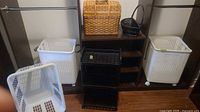 Group shot of both resin hampers, plastic laundry basket, rolling cart, lidded wicker basket and black wicker basket