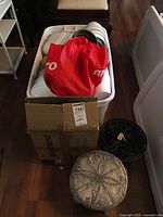 Tote filled with white plastic pots, red bag on top, cardboard box and knit item in foreground