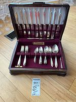Open flatware case showing knives in lid, forks and spoons in base, and auction tag