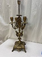 full view of brass candelabra showing three candle cups, central finial and footed base