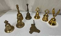 Group shot of all 8 brass bells and brass teddy bear keychain