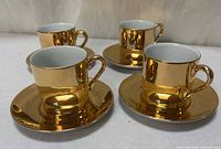 Group view of four gold demitasse cups on saucers