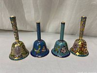 Four cloisonné enamel bells standing upright showing full bodies and handles