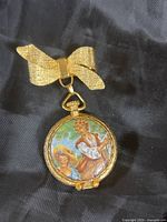 Full view of gold-tone perfume container with bow hanger