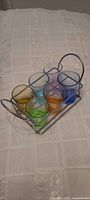 six colored shot glasses seated in chrome wire caddy on fabric surface